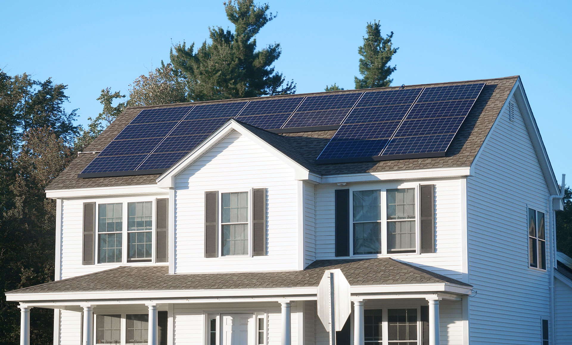 A two-story home with white siding and solar panels ont he roof