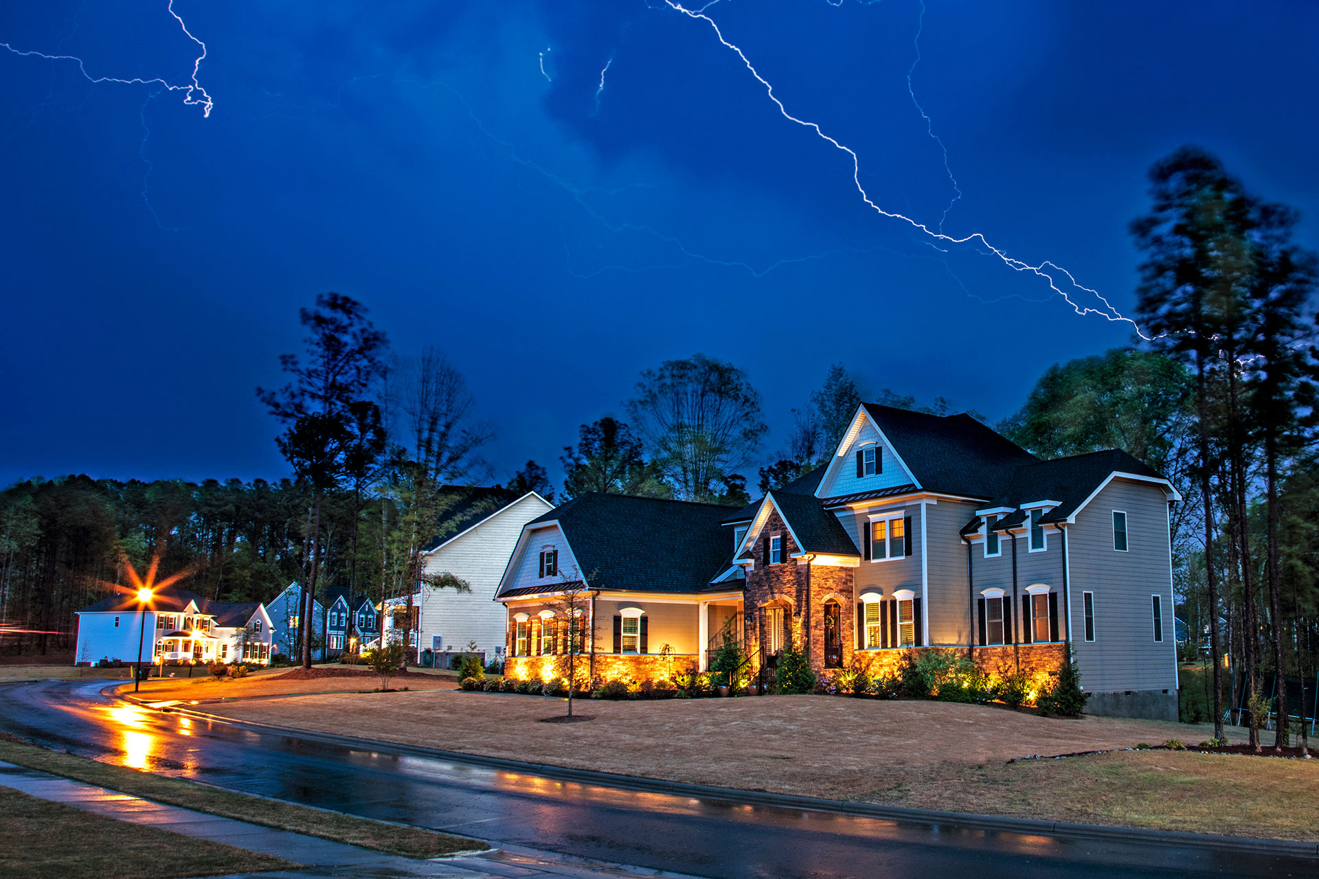 A lightning bolt flashes across the sky during a storm, but the house in the forefront is still lit with power thanks to a generator